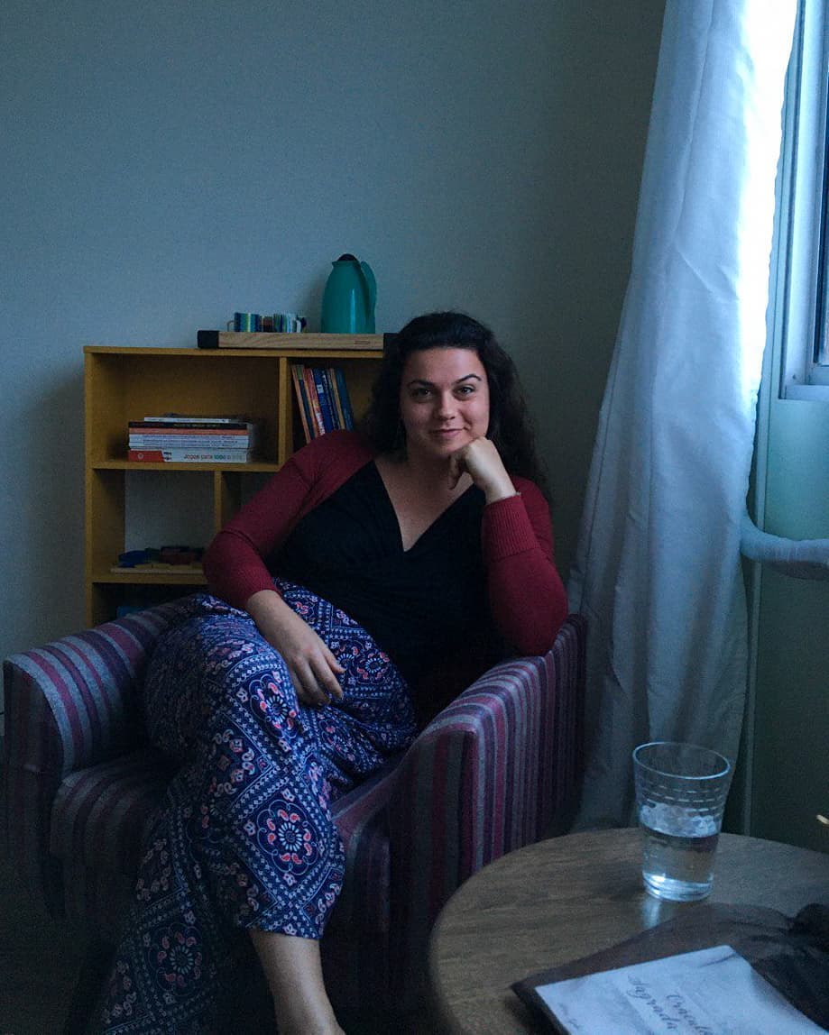 Aline Ferreira Gomes sentada em poltrona, mão apoiada no rosto, retrato profissional em ambiente acolhedor